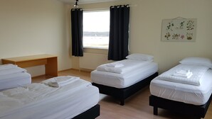 A hotel room with three single beds, a wooden desk, and a window with black curtains. - Húsabakki Guesthouse (Dalvik)