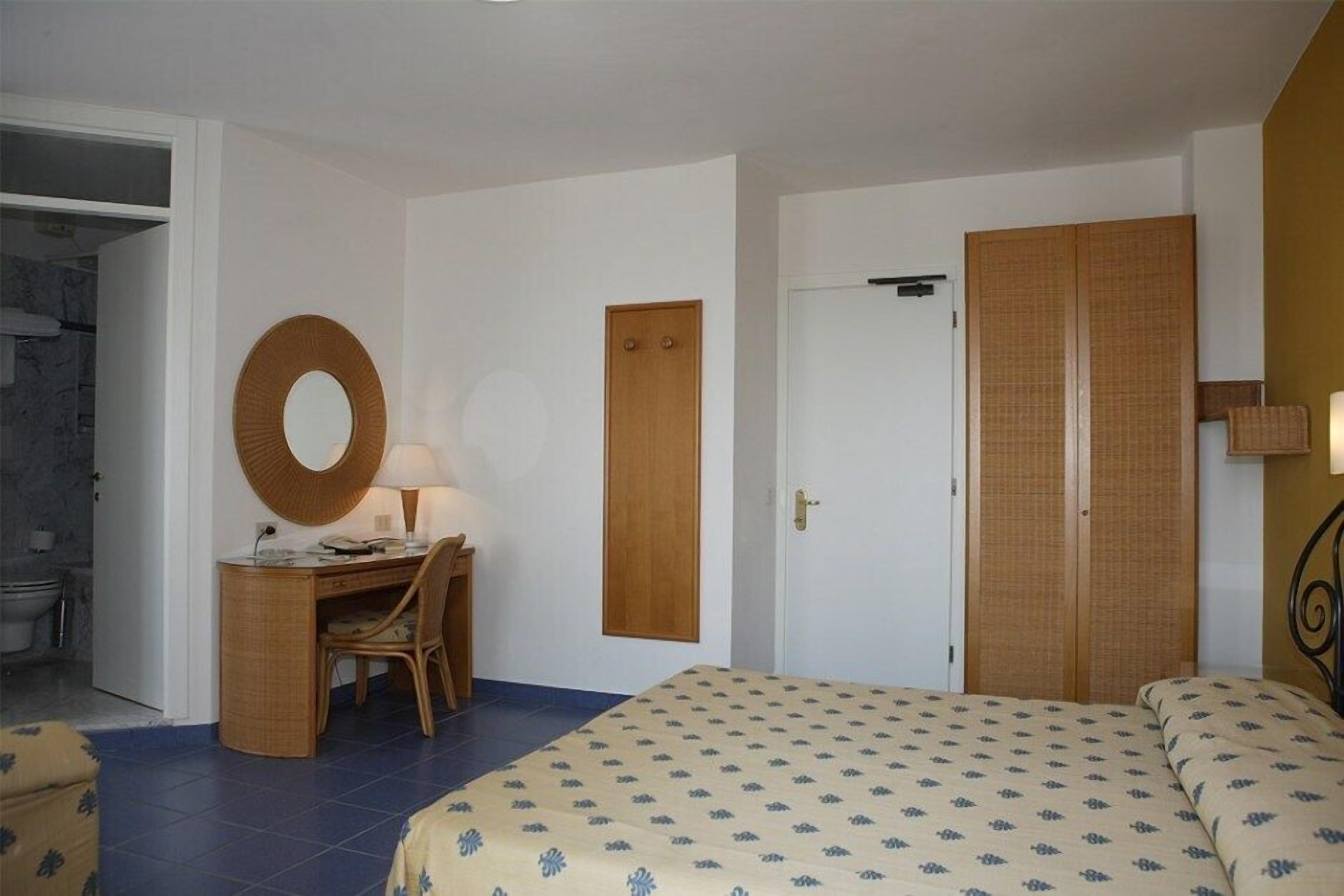 Ein Schlafzimmer mit einem Bett, einem Schreibtisch mit Stuhl, einem runden Spiegel und einem Kleiderschrank.