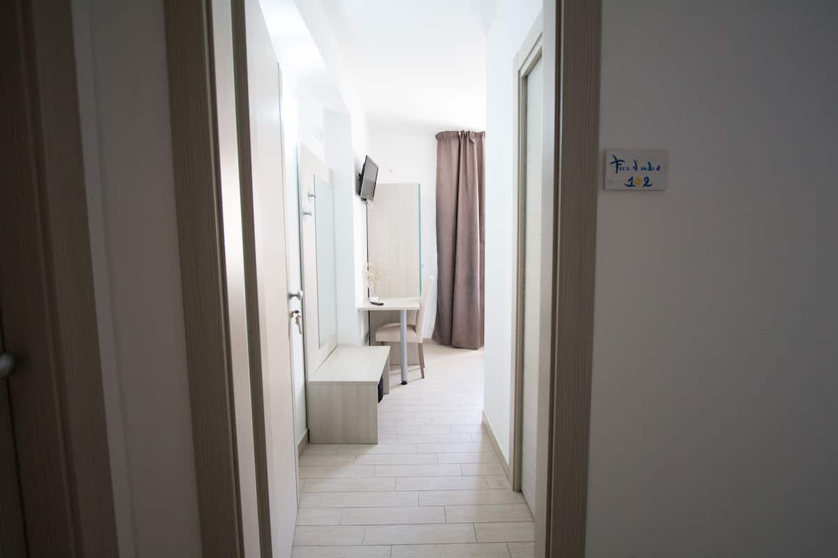 A narrow hallway with a desk, a chair, and a small bench. There is a sign on the wall and a door on the right.