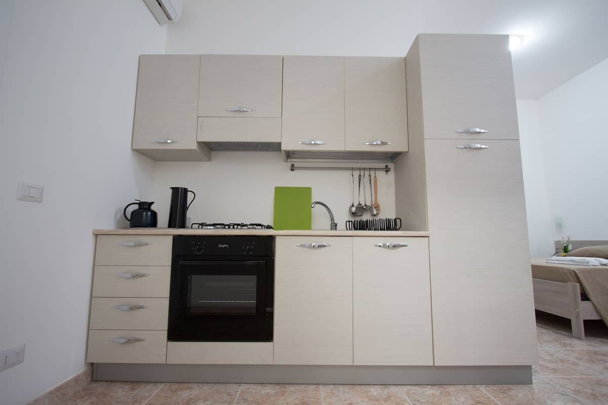 A compact kitchen with a built-in oven, a coffee maker, and a green cutting board.