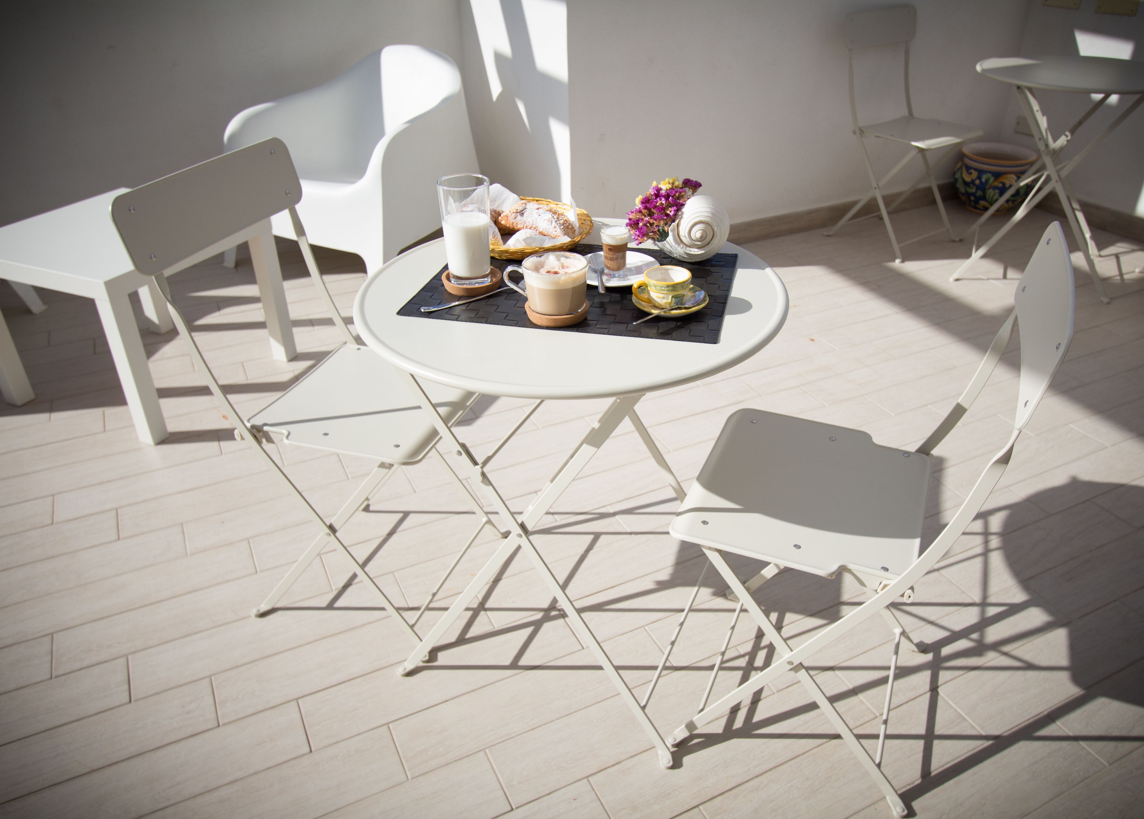 A round table with a white tablecloth, surrounded by white chairs, and a small decorative vase with purple flowers.