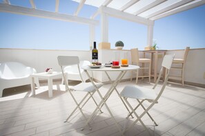 En takterrass med ett bord dukat för två personer, vita stolar, en flaska vin och ett glas apelsinjuice.