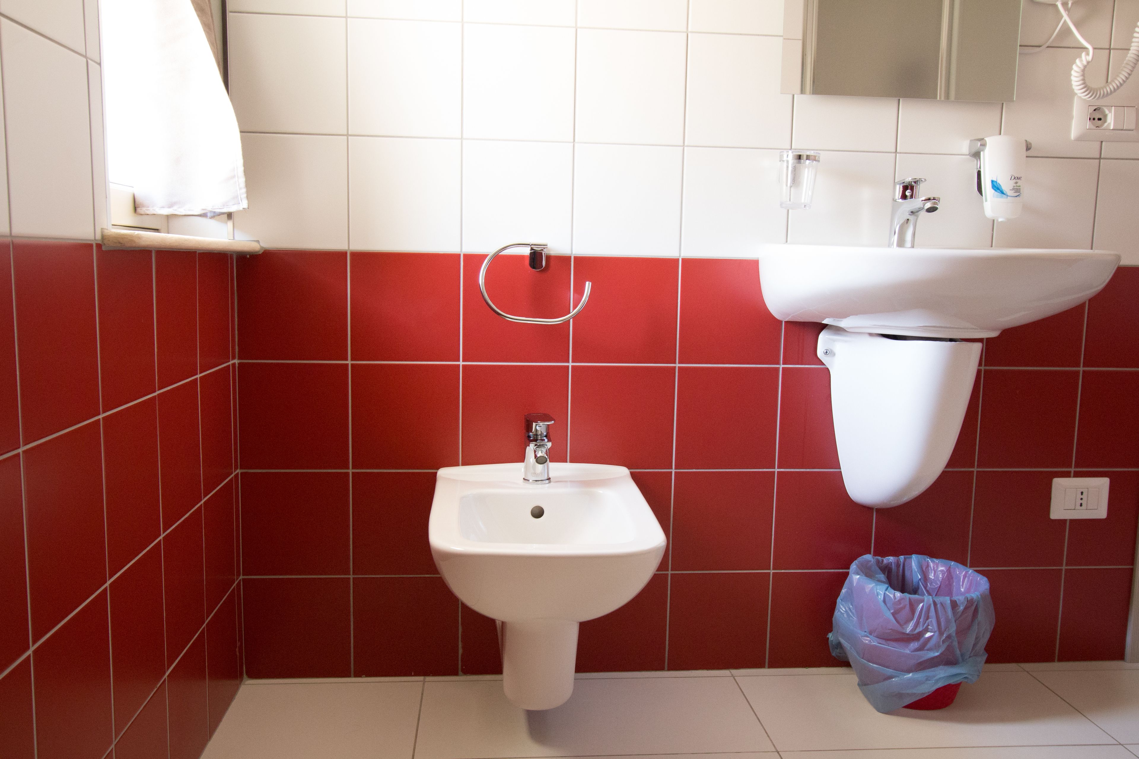 Une salle de bain avec un lavabo blanc, des carreaux rouges, un porte-serviettes et une poubelle.