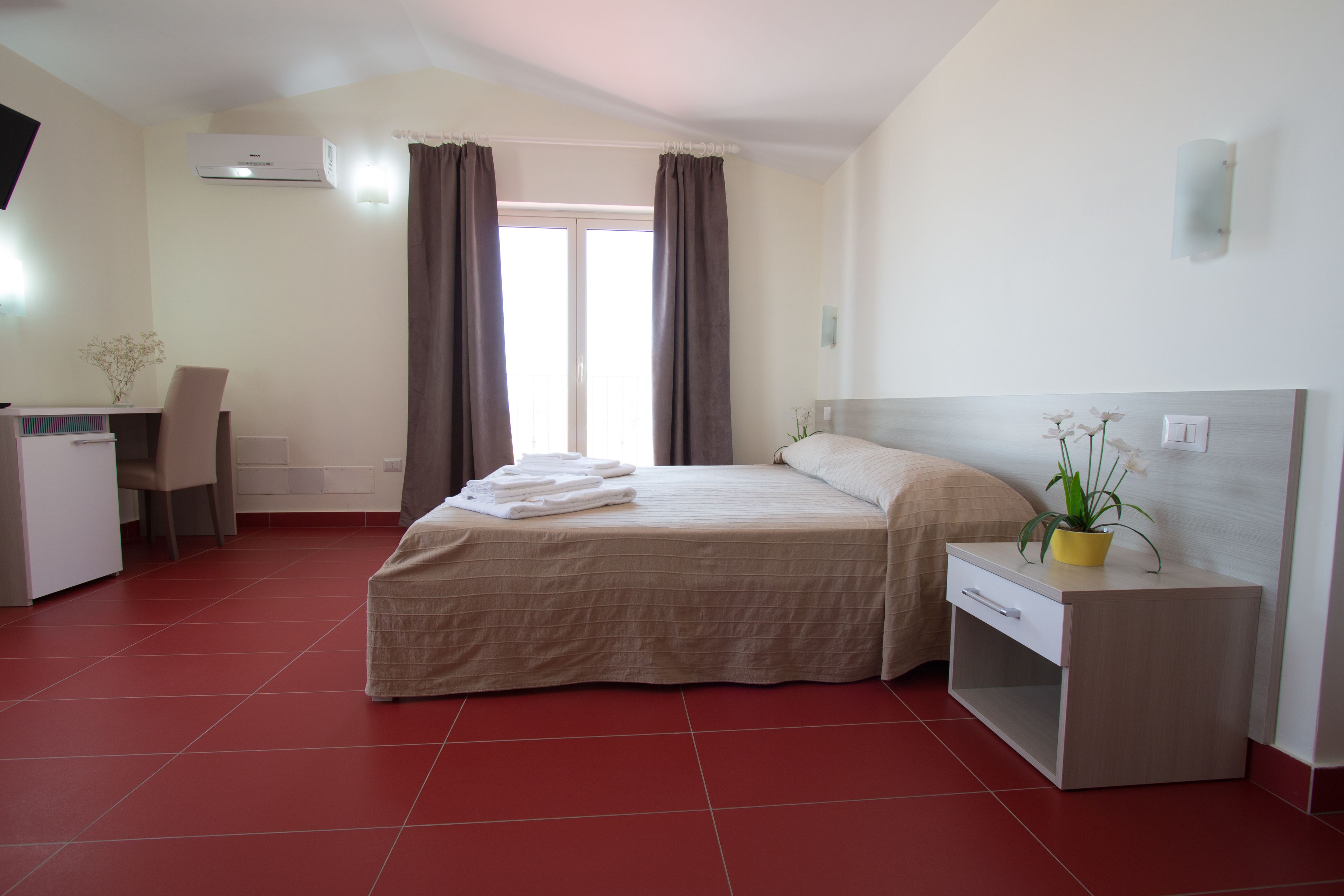 Habitación de hotel con cama, escritorio, silla, mesita de noche y planta en maceta.