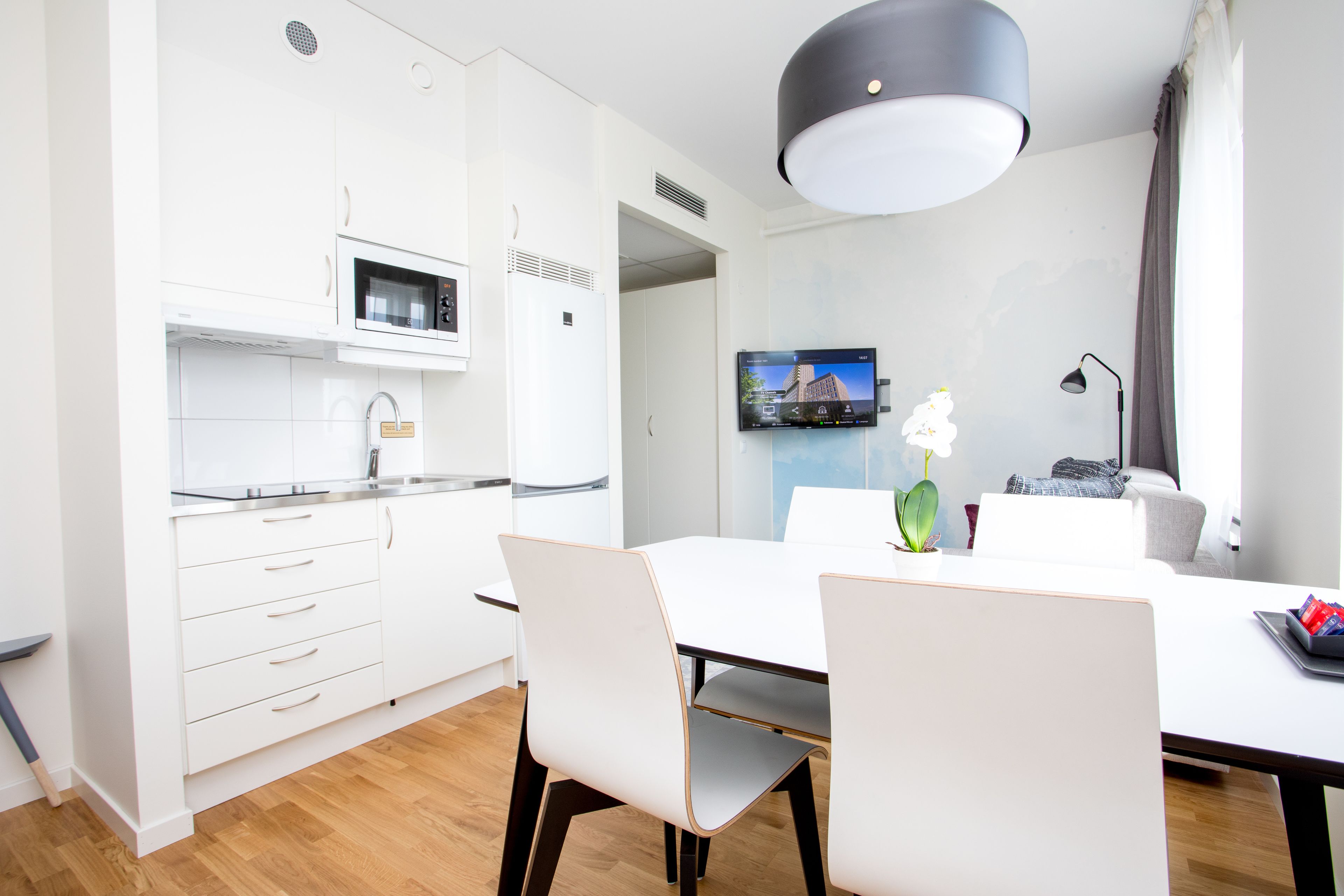 Una cocina moderna con armarios blancos, un microondas y un comedor con mesa y sillas blancas.