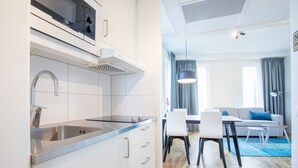 A modern kitchen with a stainless steel sink and a dining area with a gray sofa and a blue rug. - ApartDirect Älvsjö (Älvsjö)