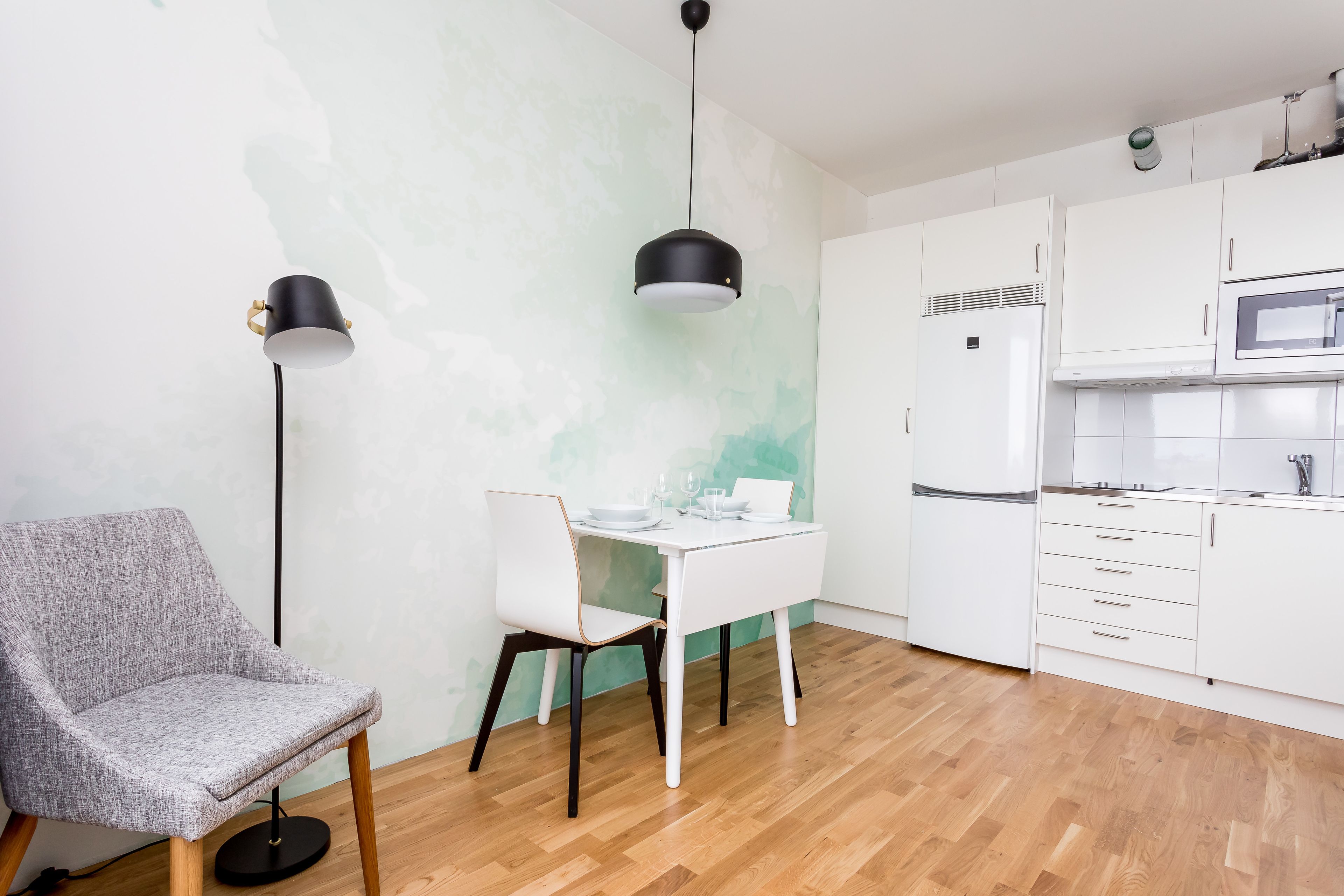 Une cuisine moderne avec des meubles blancs, une table à manger blanche et deux suspensions noires.