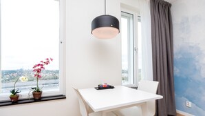A modern dining area with a white table, two chairs, a black pendant light, and two potted plants on the windowsill. - ApartDirect Älvsjö (Älvsjö)