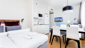 A modern hotel room with a bed, a desk, a dining table, and a kitchen area. - ApartDirect Älvsjö (Älvsjö)