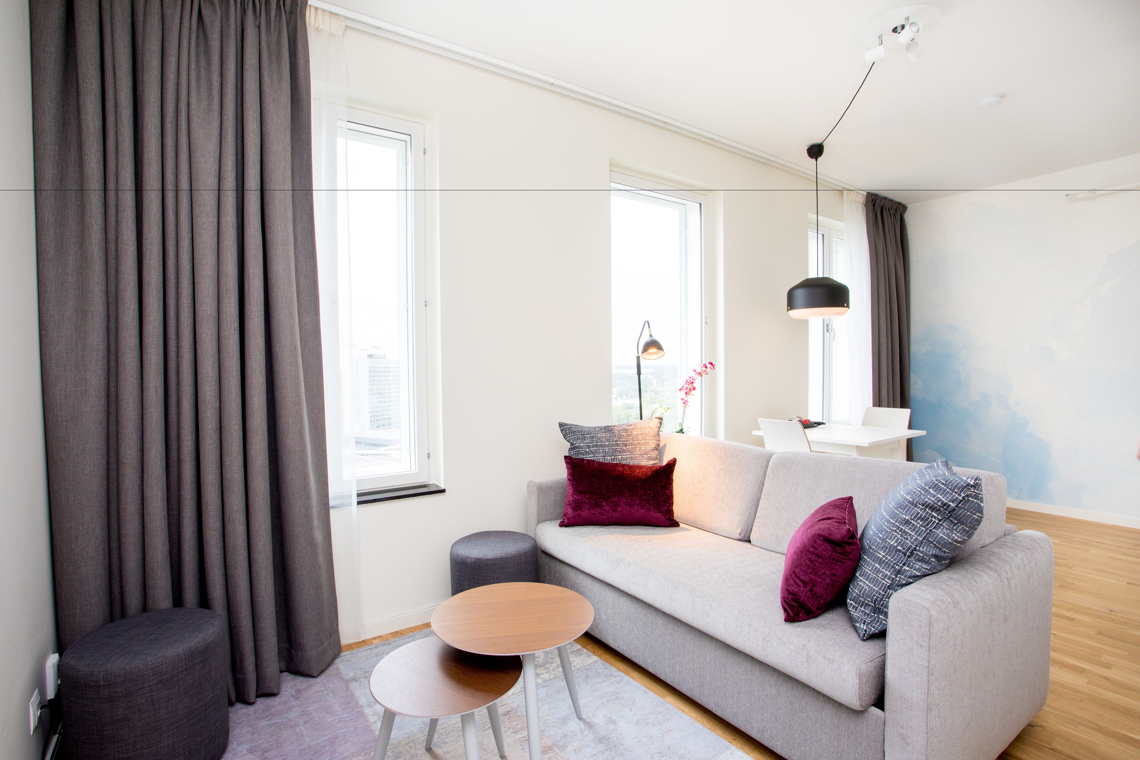A modern living room with a grey sofa, round wooden coffee table, and a grey ottoman.