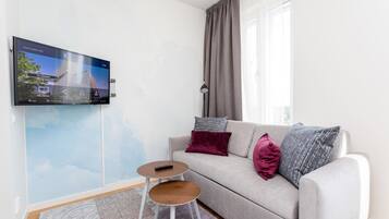 Ett modernt vardagsrum med en grå soffa, två sidobord, en väggmonterad TV och en mönstrad matta.