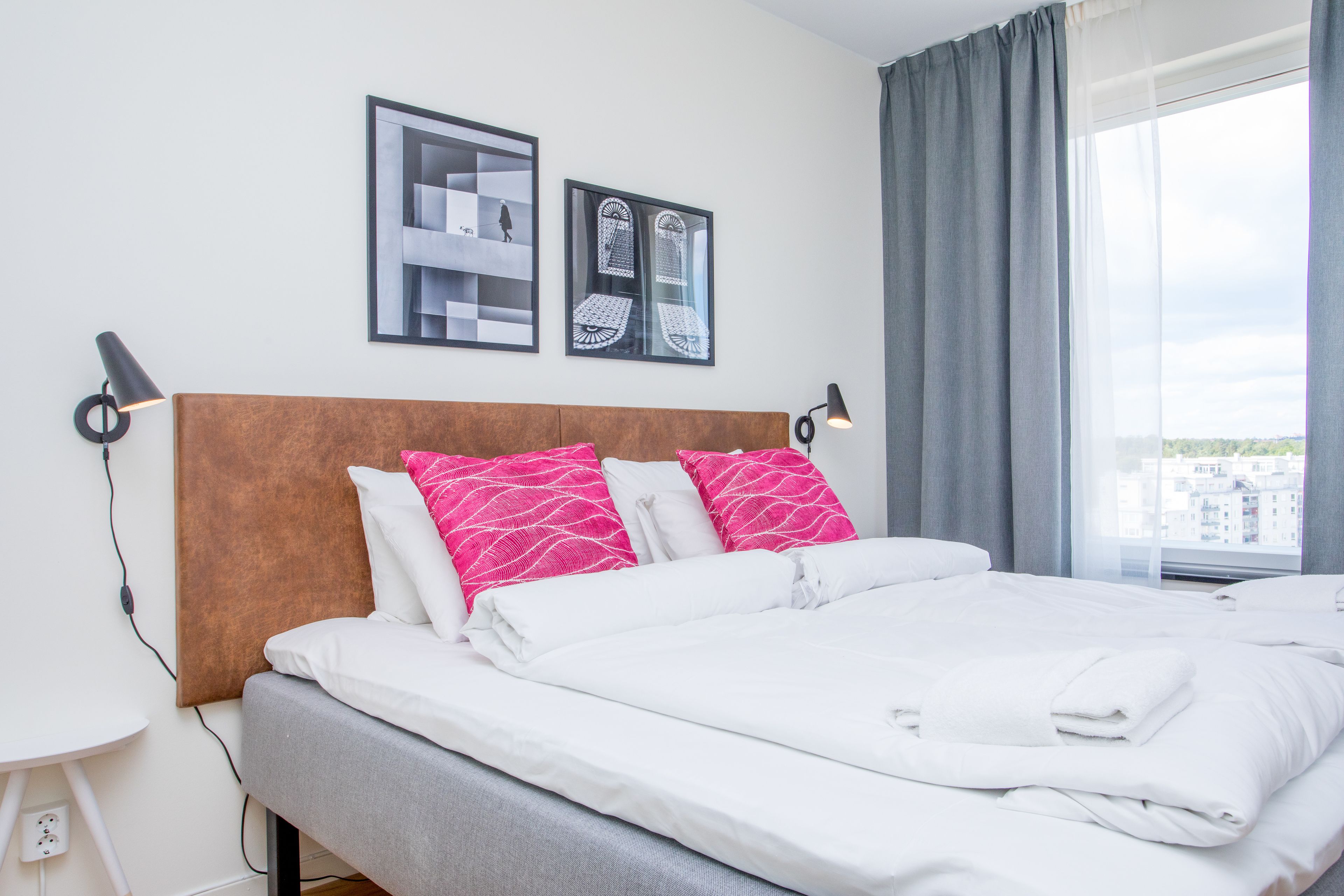 A neatly made bed with white and pink pillows, a wooden headboard, and two framed pictures on the wall.