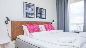 A neatly made bed with white and pink pillows, a wooden headboard, and two framed pictures on the wall.