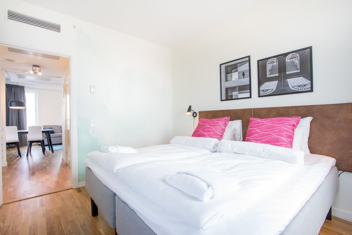 Una habitación de hotel con una cama grande, un cabecero de madera, un escritorio y sillas. Hay dos cuadros en la pared.