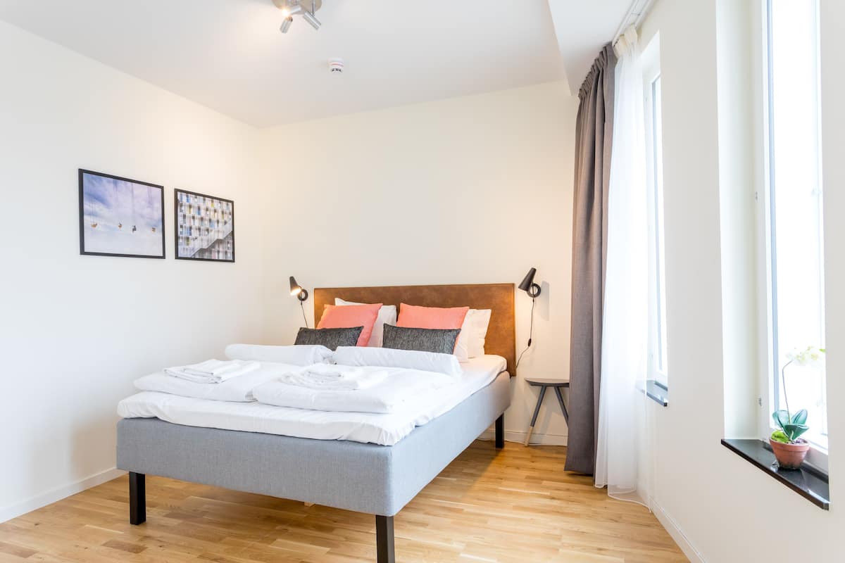 Una cama bien hecha con almohadas, una mesita de noche y una ventana con cortinas.