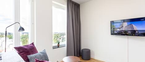 A modern living room with a grey sofa, a small round table, and a TV mounted on the wall displaying a cityscape.