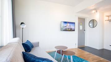 A modern living room with a sofa, two small tables, a large mirror, and a television on the wall.