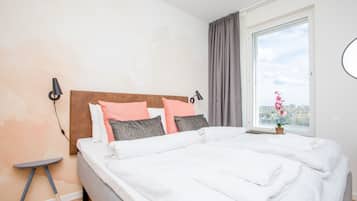 A neatly made bed with white linens, a headboard with a brown panel, and a window with a view of a cityscape.