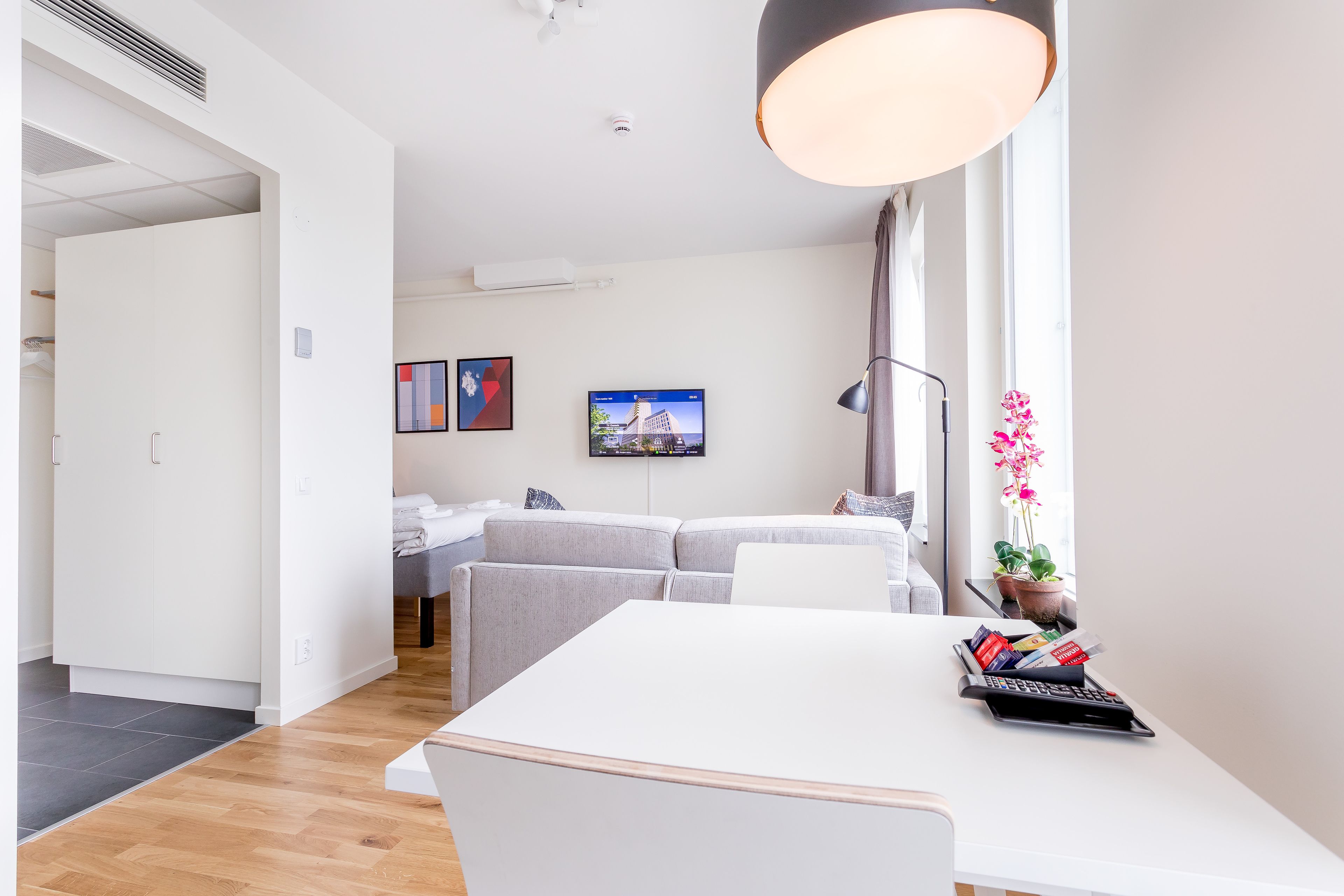 A modern living room with a white sofa, a dining table, and a TV mounted on the wall.
