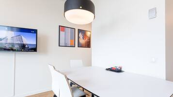 A modern conference room with a large table, white chairs, a mounted flat-screen TV, and two framed artworks on the wall.