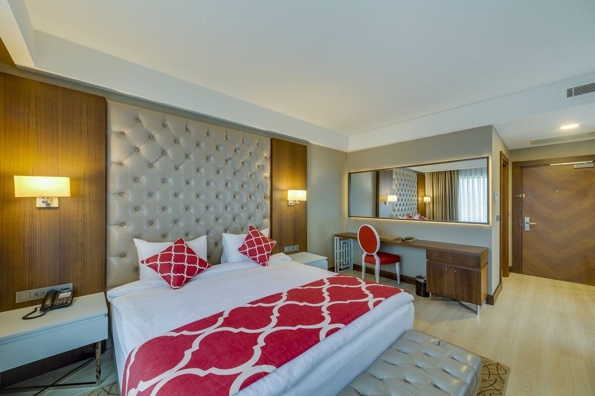 Una habitación de hotel con una cama grande, un escritorio, un espejo y un armario.