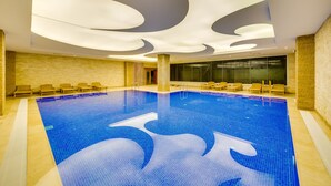 A large indoor swimming pool with a blue wave design on the floor, surrounded by lounge chairs and a modern ceiling with recessed lighting. - Demircioğlu Park Hotel (Mugla)