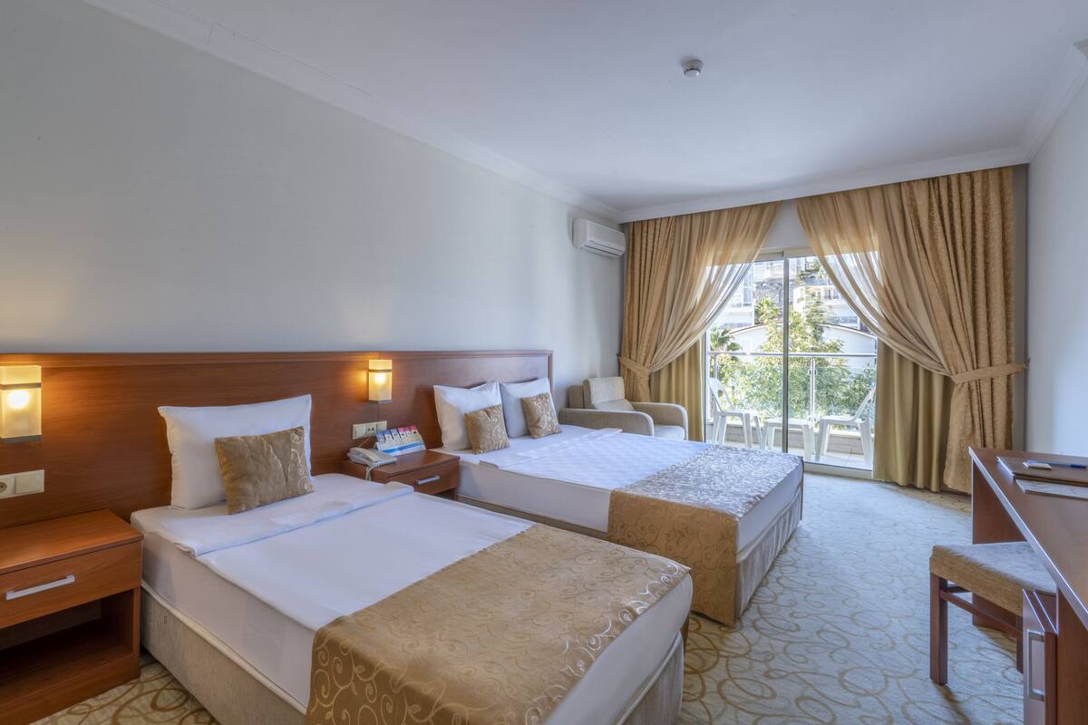 Habitación de hotel con dos camas, un escritorio, una silla y un ventanal con cortinas.