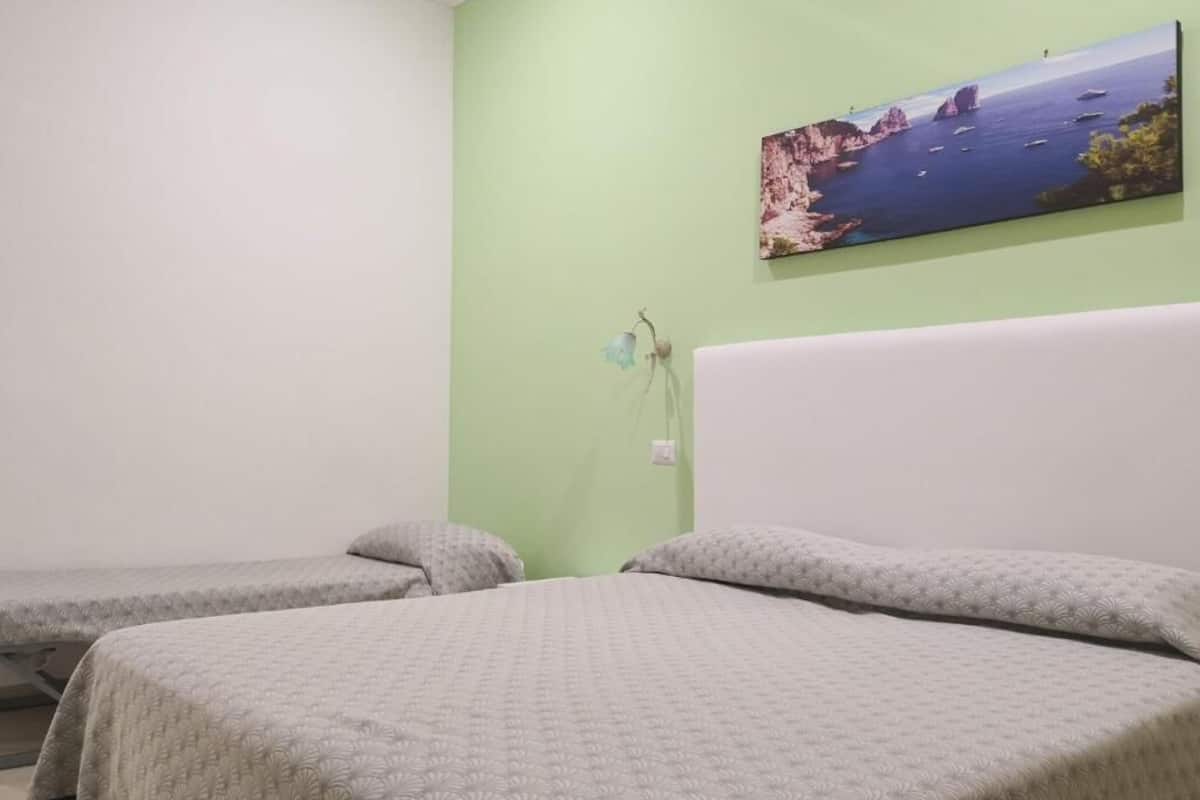 Una habitación con dos camas individuales, una pared verde y un cuadro con una escena costera.
