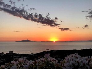 A sunset over a calm sea with a distant island and a coastal town. - Terrazza Iride (Massa Lubrense)