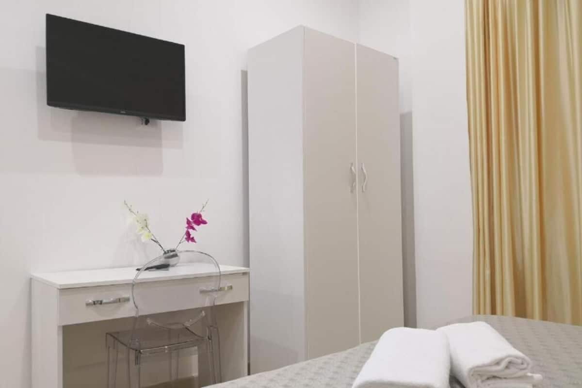 Habitación de hotel con cama, escritorio, silla, armario, televisión de pantalla plana y cortina.