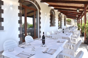 A covered outdoor dining area with white tables and chairs, stone walls, and arched windows. - Terrazza Iride (Massa Lubrense)