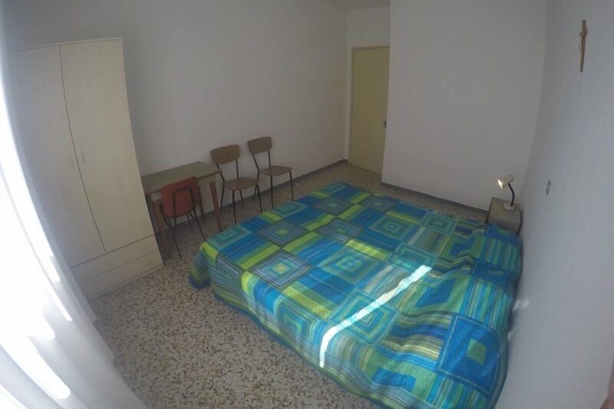Een kleine, eenvoudig ingerichte kamer met een bed, een bureau, twee stoelen en een kledingkast.