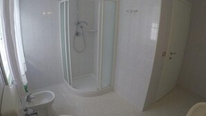 Ett modernt badrum med en dusch som är avskärmad med glasväggar, ett handfat och en toalett.