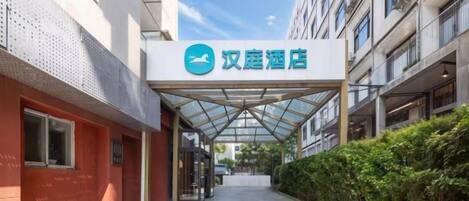 A hotel entrance with a covered walkway, a sign with Chinese characters, and a clear sky.