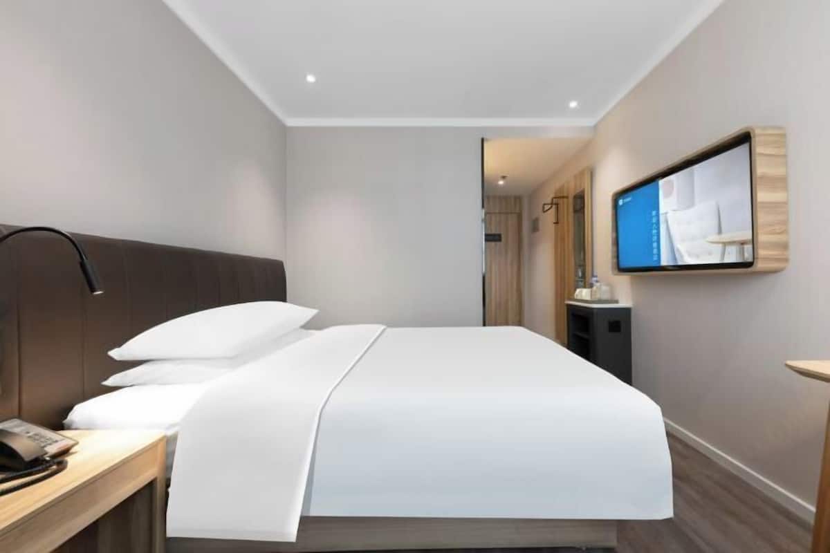 Une chambre d’hôtel comprenant un lit, une table de chevet, une lampe, un téléviseur fixé au mur et une petite table avec une chaise.