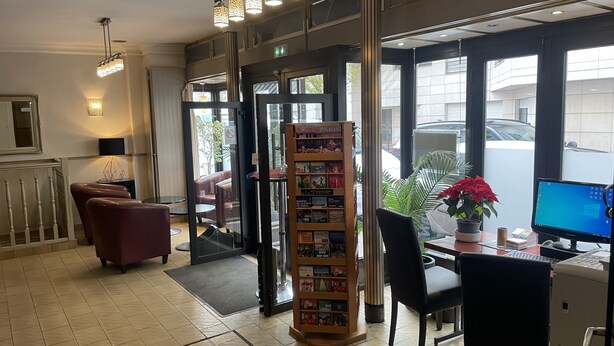 A reception area with a computer desk, a bookshelf, and a seating area with chairs. - Crystal Hotel (Levallois-Perret)