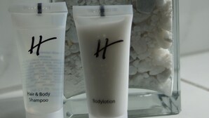 Two bottles of H shampoo and lotion on a shelf with a cactus and white pebbles in the background. - Hotel Jägerhof (Ratingen)