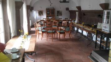 A dining area with wooden tables and chairs, a kitchen area with a stove, and a tiled floor.