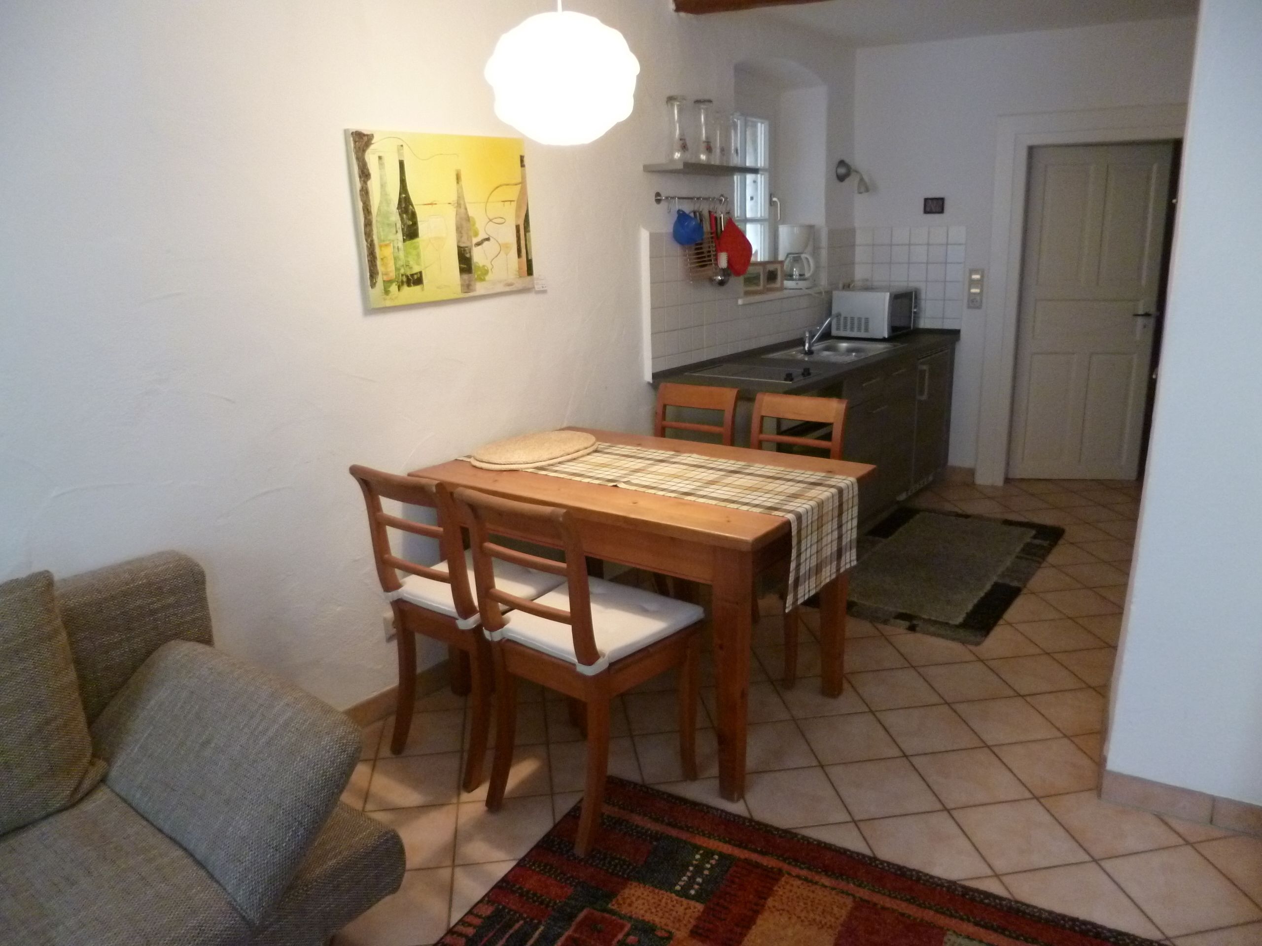 Ein gemütlicher Wohnbereich mit Esstisch, Stühlen, einer Couch, einer Küchenzeile mit Spüle und Schränken sowie einer Tür zu einem weiteren Raum.