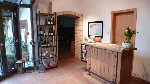 A reception area with a wooden counter, a wine rack, and a potted plant. - Alter Winzerhof Weisenheim am Berg e.K. (Weisenheim am Berg)