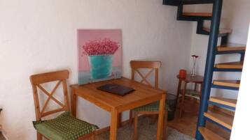 Un petit coin repas avec une table et des chaises en bois, un tableau au mur et un escalier en colimaçon.