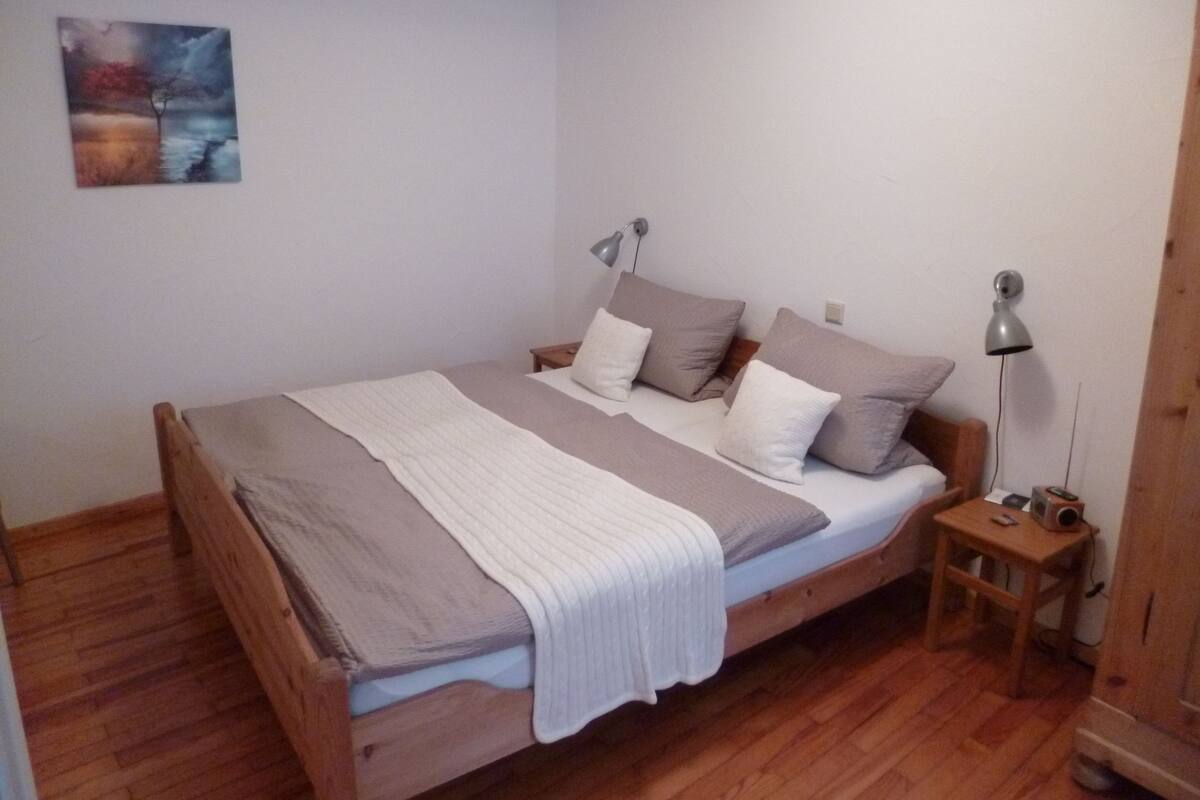 Une chambre à coucher avec un lit en bois, du linge de lit blanc et un tableau accroché au mur.