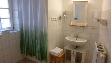 Ein Badezimmer mit Duschvorhang, Waschbecken, Spiegel und Heizkörper.