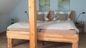 A wooden bed in a room with a sloped ceiling, a small nightstand, and a wall-mounted lamp. - Alter Winzerhof Weisenheim am Berg e.K. (Weisenheim am Berg)