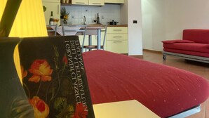 A room with a bed, a red sofa, a kitchen area, and a dining table. - Jonio Vacanze Residence (Castellaneta)