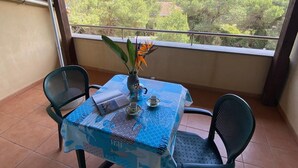 A covered patio with a table set for two, chairs, and a view of greenery and buildings. - Jonio Vacanze Residence (Castellaneta)