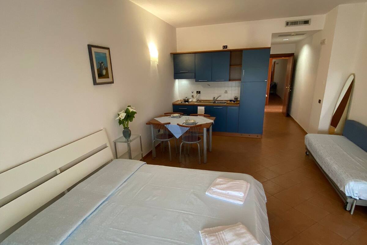 A hotel room with a bed, a small table with chairs, a kitchenette, and a bathroom.