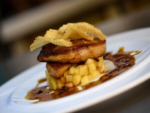 Un plat composé d’un morceau de viande, de fruits coupés en dés et d’une sauce, le tout servi dans une assiette blanche.