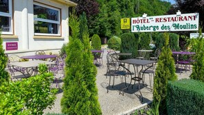 Een hotel met terras en een bordje met de tekst 'Hôtel - Restaurant L'Auberge des Moulins'.