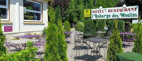 Un hotel con mesas al aire libre y un cartel que dice 'Hôtel - Restaurant L'Auberge des Moulins'.